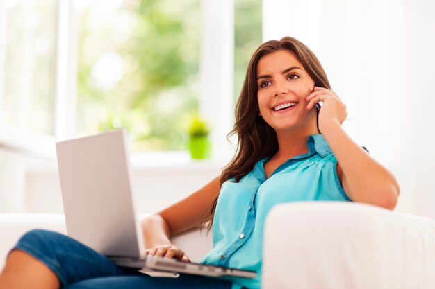 Mujer feliz pagando con laptop y hablando por teléfono móvil