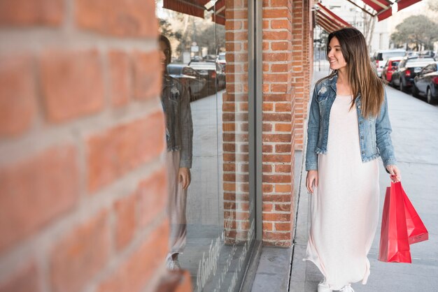 Mujer feliz con paquetes de compras caminando en la calle cerca de las ventanas de la tienda