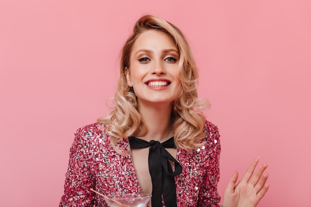 Mujer feliz en la parte superior brillante con lazo está sonriendo en la pared rosa