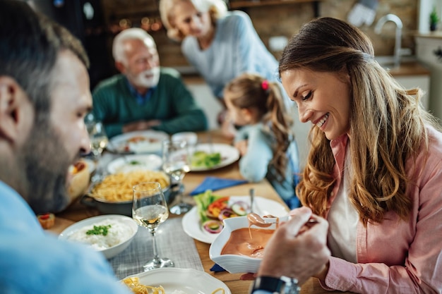 Mujer feliz pasándole comida a su esposo mientras almuerza en familia en casa