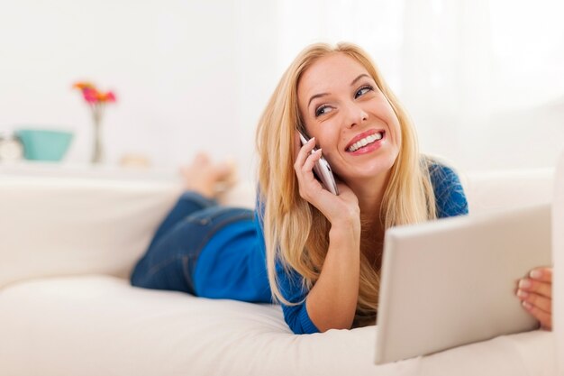 Mujer feliz pasar tiempo en el sofá con tableta digital y teléfono móvil