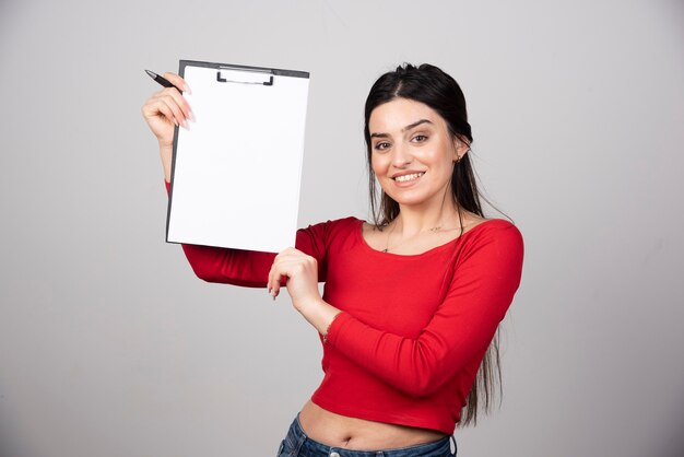 Mujer feliz con el pelo largo mostrando un portapapeles con lápiz.