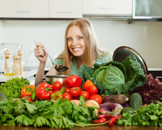 mujer feliz de pelo largo que cocina con el montón de verduras