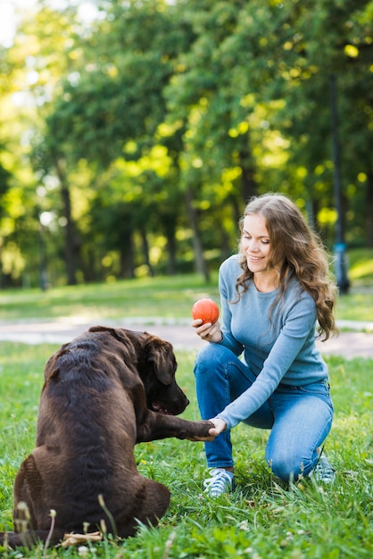 Mujer feliz con la pelota sacudiendo la pata de su perro en el parque