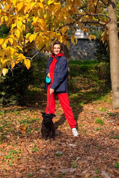 Mujer feliz con perro en el parque con hojas otoñales