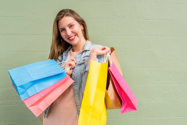 Foto gratuita mujer feliz de pie con bolsas de compras en la pared