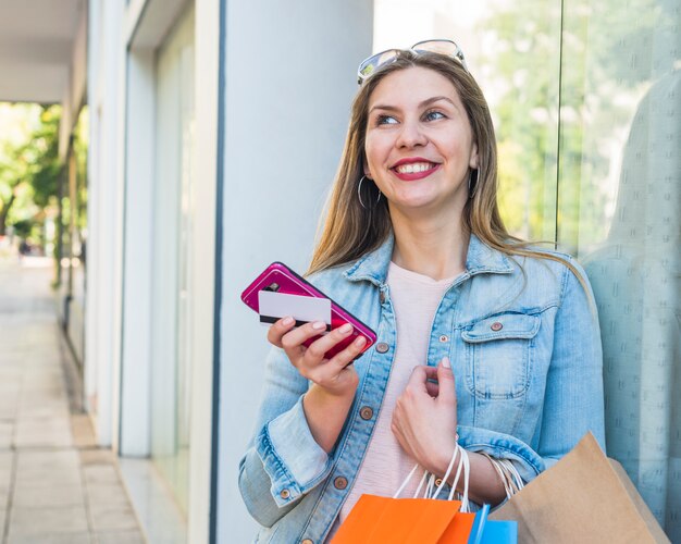 Mujer feliz de pie con bolsas, teléfono inteligente y tarjeta de crédito