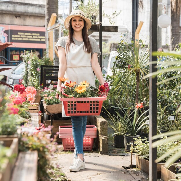 Mujer feliz de pie en invernadero con contenedor de flores frescas