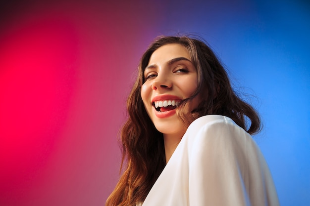 Foto gratuita mujer feliz de pie, sonriendo sobre fondo de estudio color. hermoso retrato femenino de medio cuerpo.