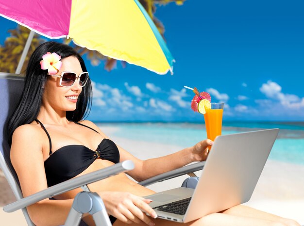 Mujer feliz en la playa con una computadora portátil.