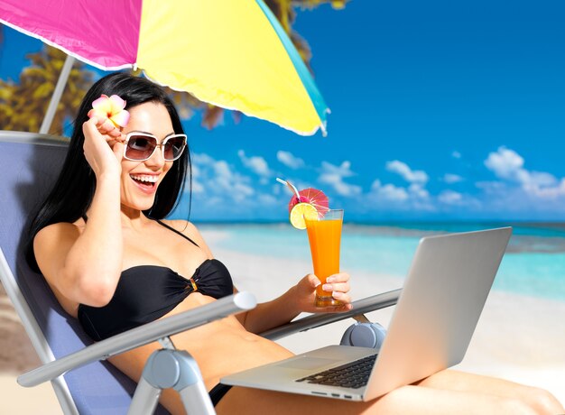 Mujer feliz en la playa con una computadora portátil.