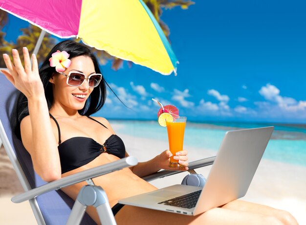 Mujer feliz en la playa con una computadora portátil.