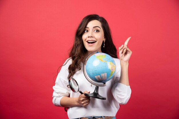 Mujer feliz posando con globo y lupa mientras apunta hacia arriba. Foto de alta calidad