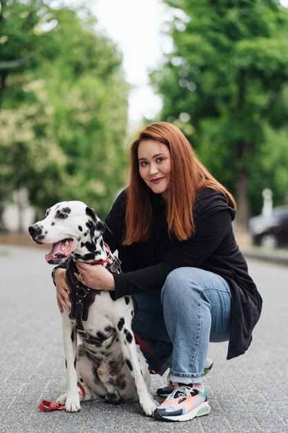 Mujer feliz posando y jugando con su perro dálmata durante un paseo por la ciudad urbana