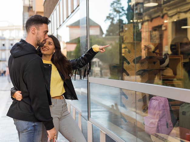 Mujer feliz que abraza y que muestra en ventana de la tienda al hombre joven