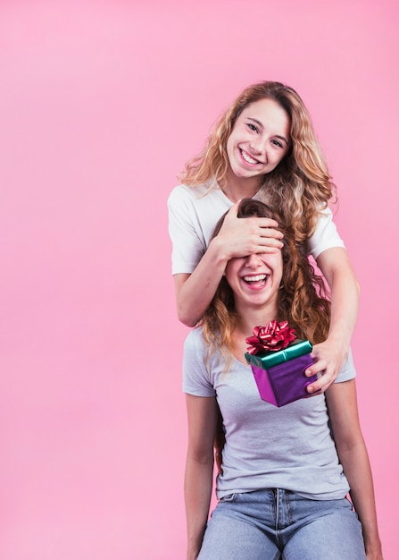 Mujer feliz que da el rectángulo de regalo a su hermana contra fondo rosado