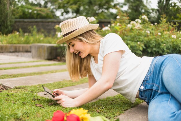 Mujer feliz que miente en hierba con la tableta