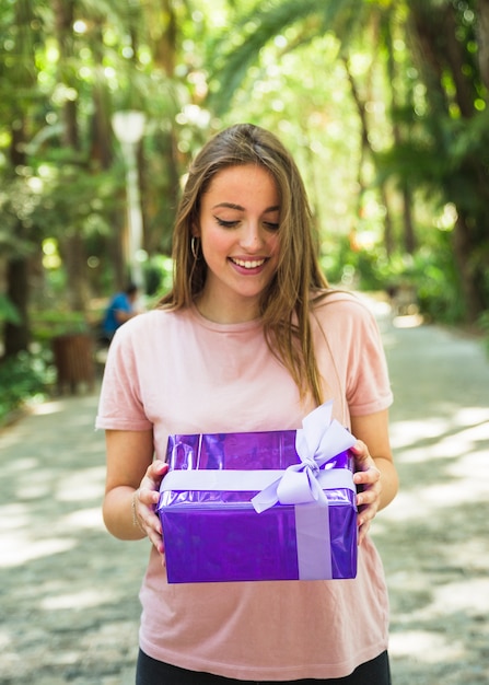 Mujer feliz que mira la caja de regalo púrpura