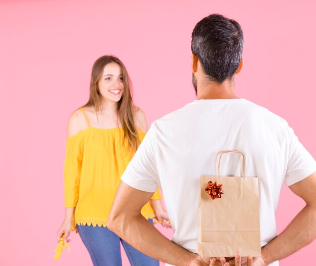 Mujer feliz que mira a su novio que sostiene las cajas de regalo contra fondo rosado