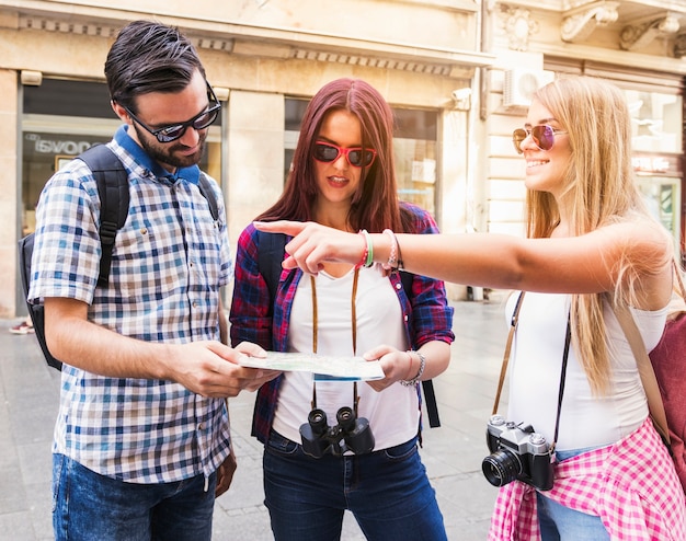 Mujer feliz que muestra la dirección a sus amigos que sostienen el mapa