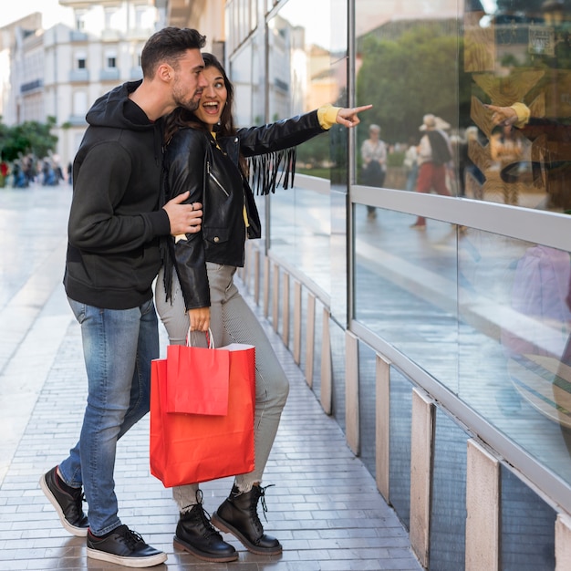 Foto gratuita mujer feliz que muestra en la ventana de la tienda al joven