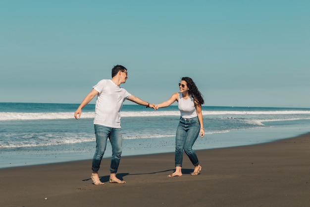 Mujer feliz que quiere que el hombre siga al agua en la playa