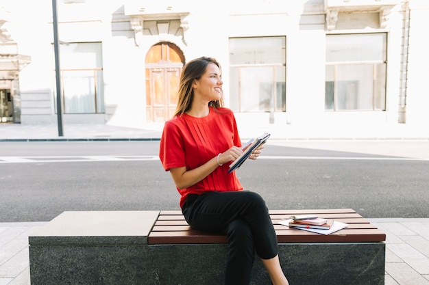 Mujer feliz que se sienta en banco con el diario