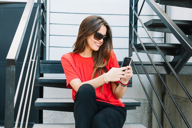 Mujer feliz que se sienta en la escalera usando el teléfono móvil