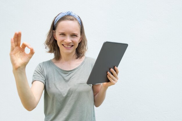 Mujer feliz que sostiene el artilugio, usando la PC de la tableta