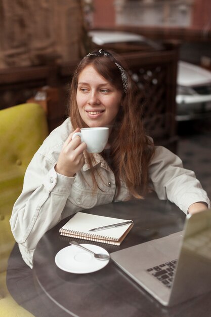 Mujer feliz que sostiene el café cerca de ventana