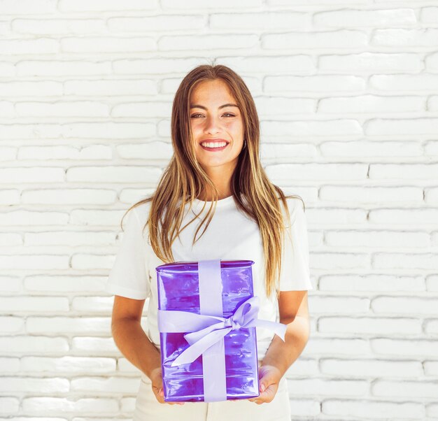 Mujer feliz que sostiene la caja de regalo contra la pared de ladrillo