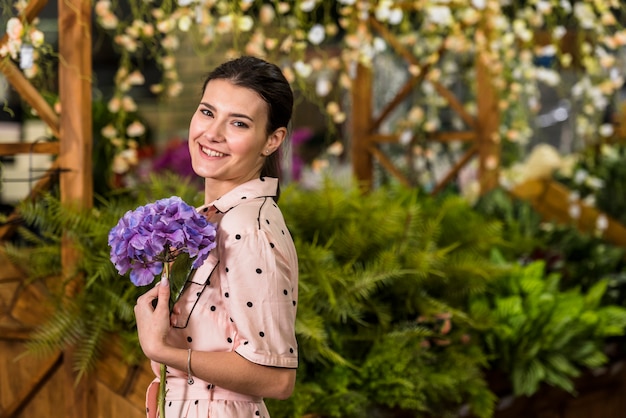 Foto gratuita mujer feliz que sostiene la flor azul en casa verde