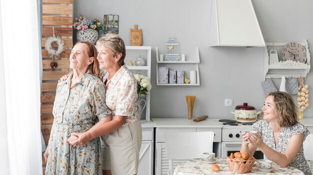 Mujer feliz que sostiene la taza de café que mira a su madre y magnífico