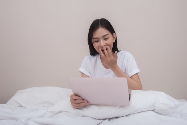 Mujer feliz que usa la computadora portátil que sonríe que se sienta en cama