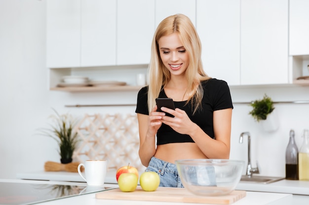 Mujer feliz que usa el teléfono en cocina