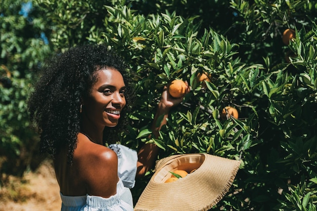 Mujer feliz recogiendo fruta naranja en el jardín