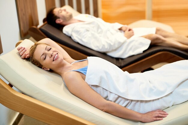Mujer feliz relajándose con su esposo en sillones mientras pasa un día en el spa de salud