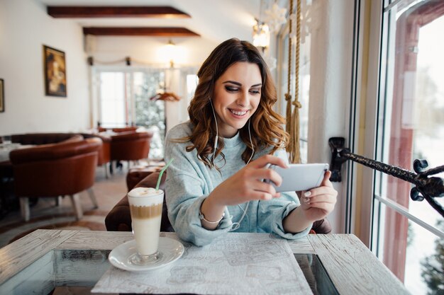 Mujer feliz con rizos en café con teléfono inteligente y sonriendo
