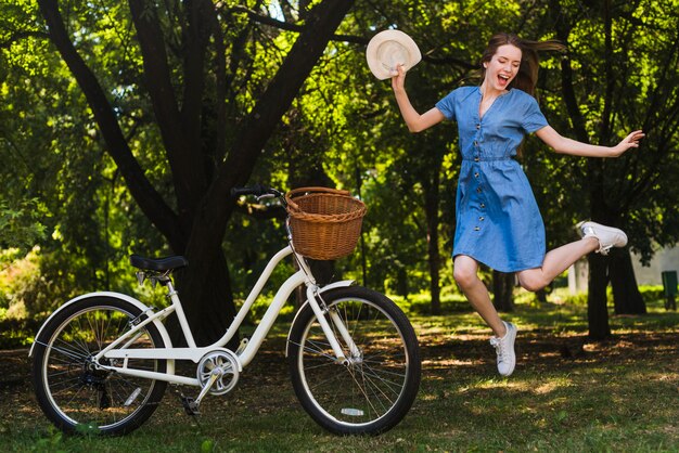 Mujer feliz saltando al lado de bicicleta