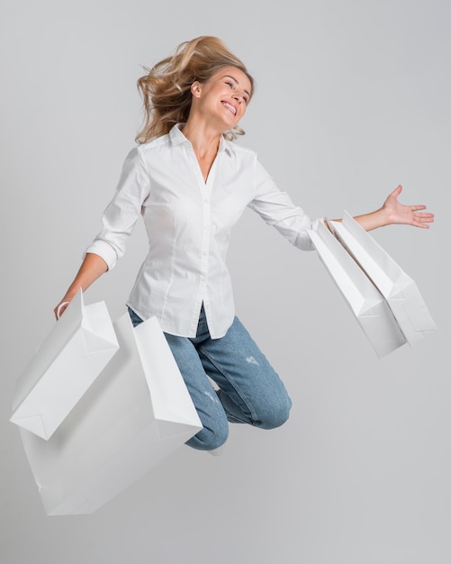 Mujer feliz saltando y posando mientras sostiene un montón de bolsas de la compra.