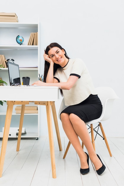 Mujer feliz sentada a la mesa con laptop