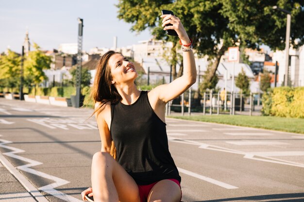 Mujer feliz sentada en patineta tomando selfie con celular