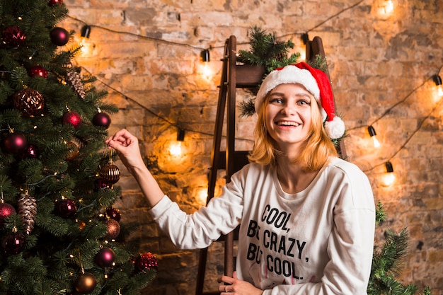 Mujer feliz en silla al lado de árbol de navidad