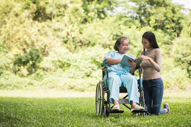 Mujer feliz en una silla de ruedas leyendo un libro con su hija en el parque