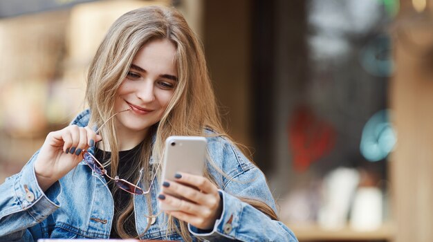 Mujer feliz con smartphone en café de comida rápida de la calle, sonriendo w