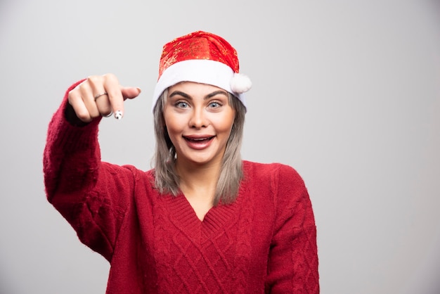 Mujer feliz con sombrero de Santa posando sobre fondo gris.