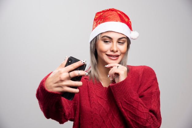 Mujer feliz con sombrero de Santa tomando fotos de sí misma.