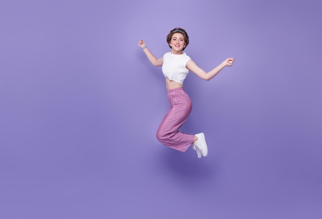 Mujer feliz sonriendo y saltando mientras celebra el éxito aislado en el fondo violeta