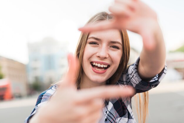 Mujer feliz sonriente que mira a través de marco de la mano