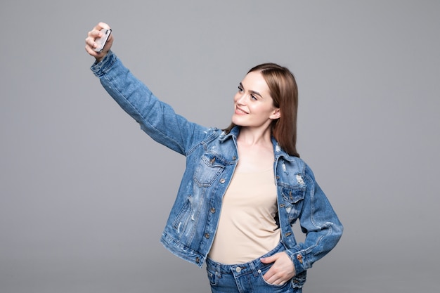 Foto gratuita mujer feliz con una sonrisa radiante haciendo selfie aislado en la pared gris